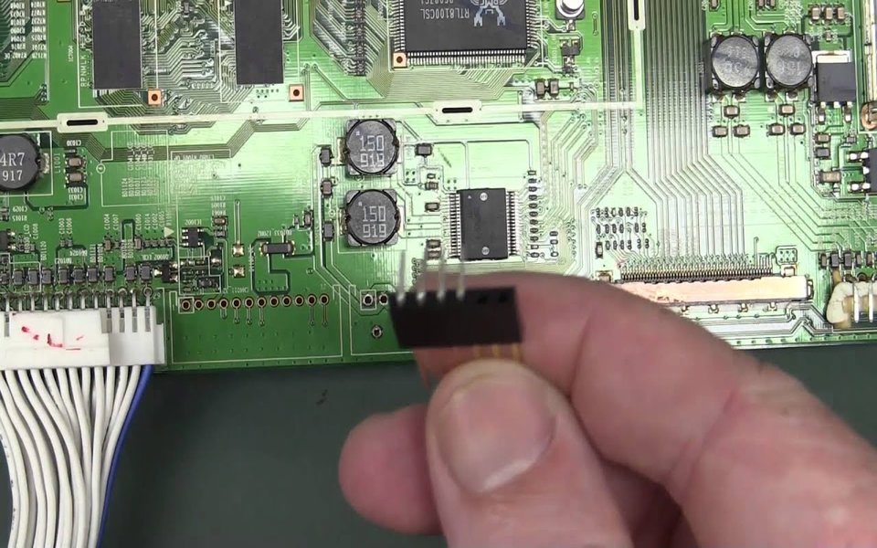 Technician holding a ribbon connector over a green circuit board